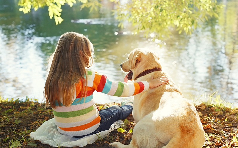 child sitting with dog at river bank